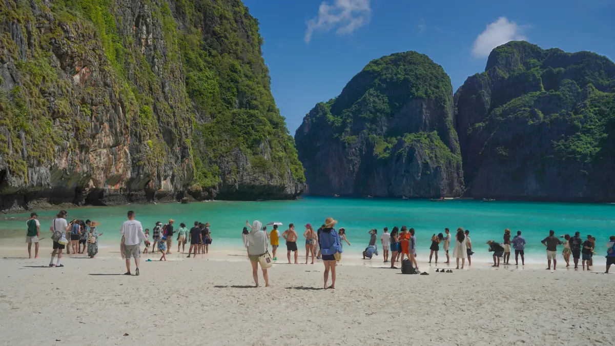 Visitors on the picturesque beach of Maya Bay in Thailand, surrounded by lush cliffs and turquoise waters.