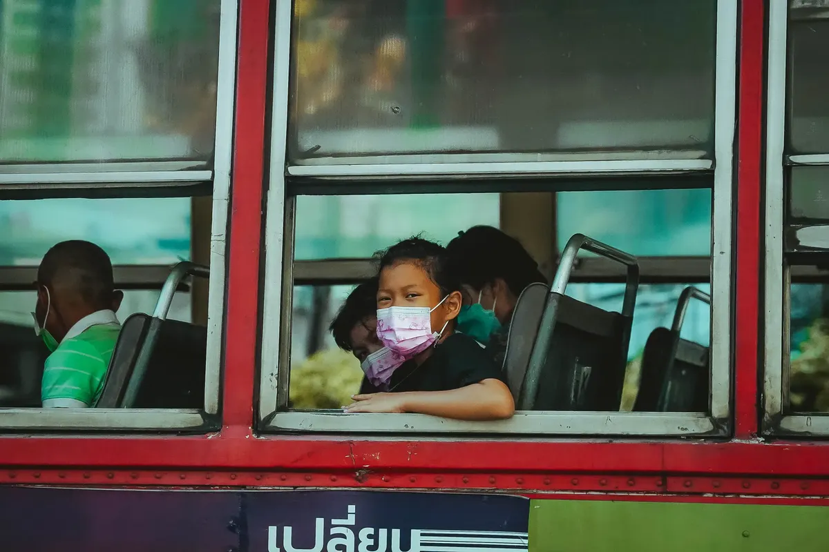 A young child wearing a face mask on a bus in Bangkok, Thailand, highlighting public transportation during pandemic times.