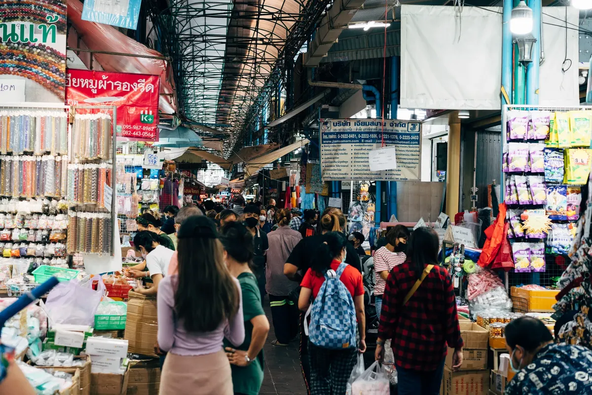 A crowded market in Bangkok with people shopping at various stalls, showcasing vibrant local culture.