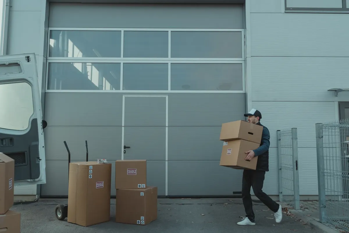 A delivery person carrying cardboard boxes outside a warehouse facility.