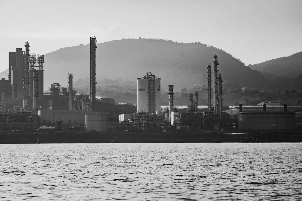 Monochrome view of an industrial complex with hills in the background, captured during the day.